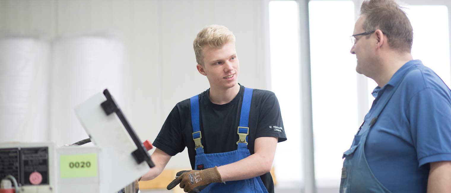 Auszubildender in Werkstatt und Ausbilder unterhalten sich