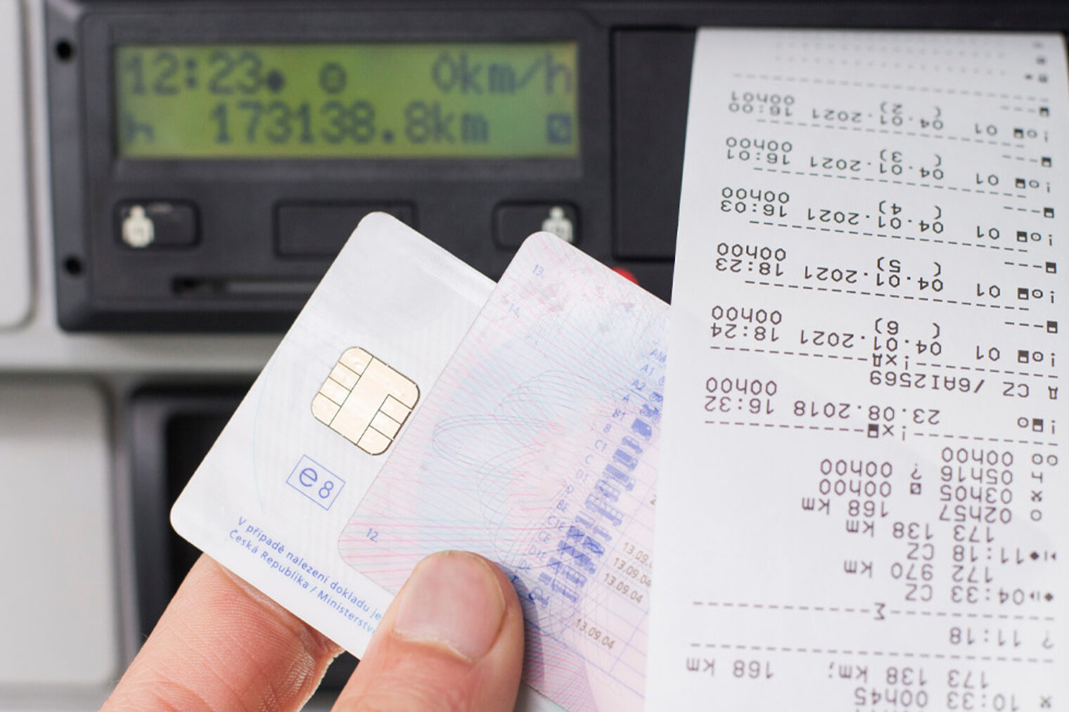 Nahaufnahme einer Hand vor einem digitalen Tachografen mit Karte und Ausdrucken
