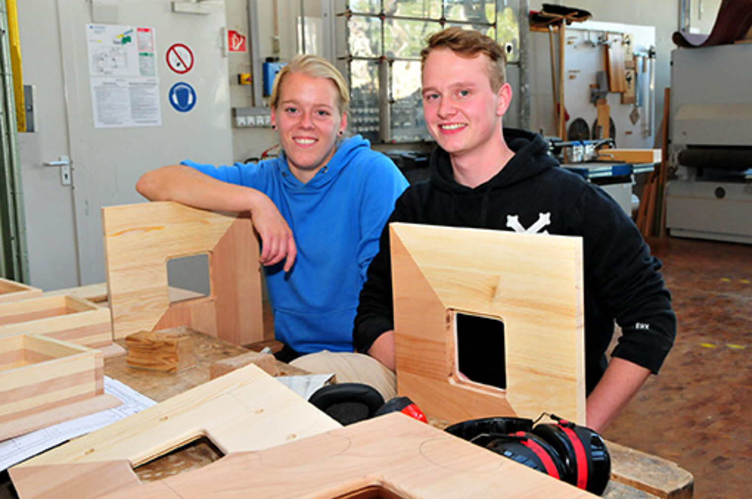 Veronika und Lukas, Auszubildende Schreiner in einer Werkstatt mit Holz-Arbeitsstücken