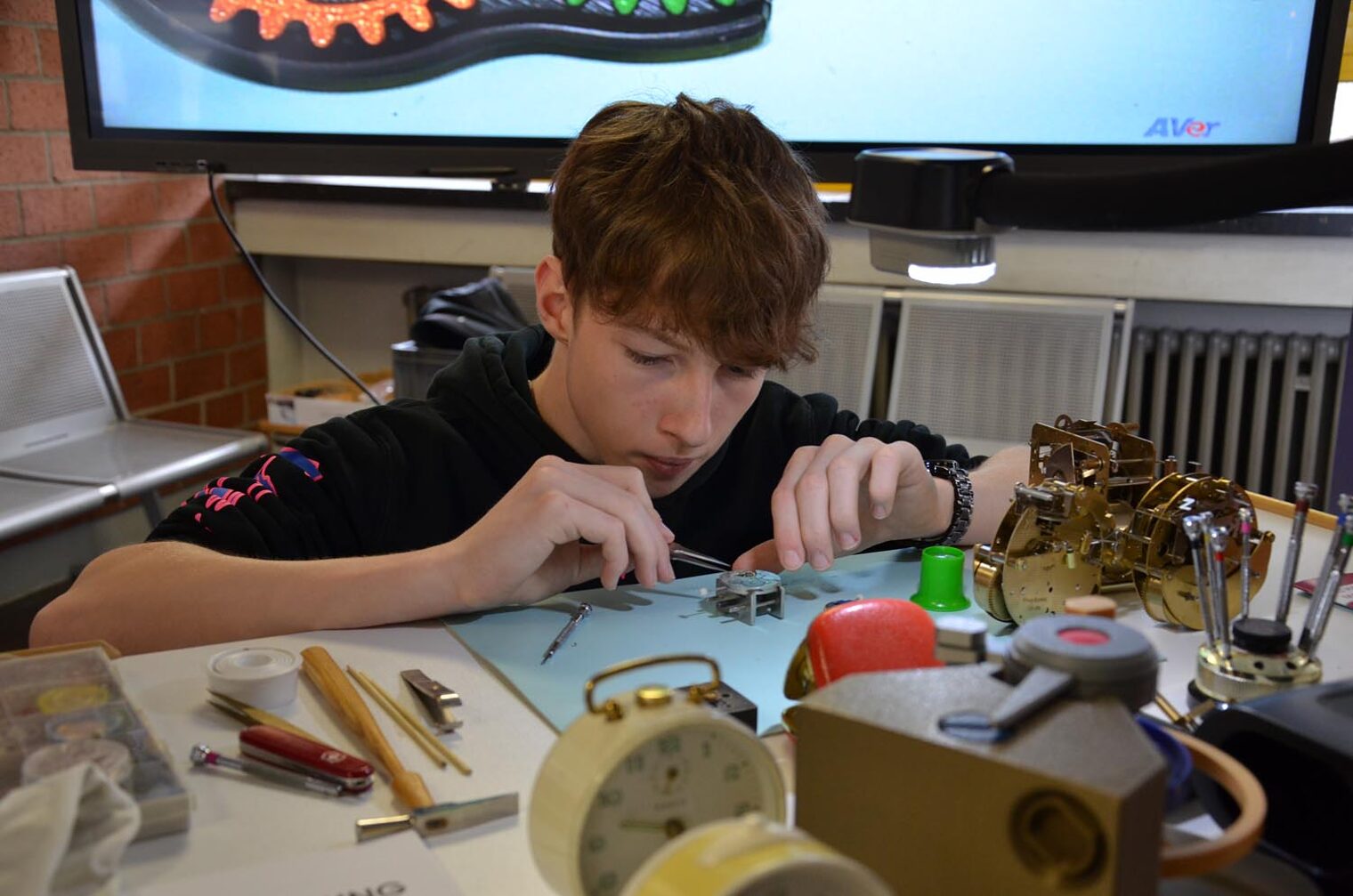 Ausprobieren des Uhrmacher-Berufs Schüler arbeitet an Uhrmechanik mit Pinzette an Tisch mit Werkzeugen