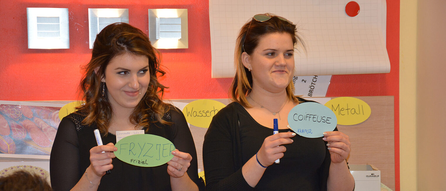 Junghandwerkeraustausch 2 Frauen halten Karten mit Berufen auf polnisch und französisch in die Luft