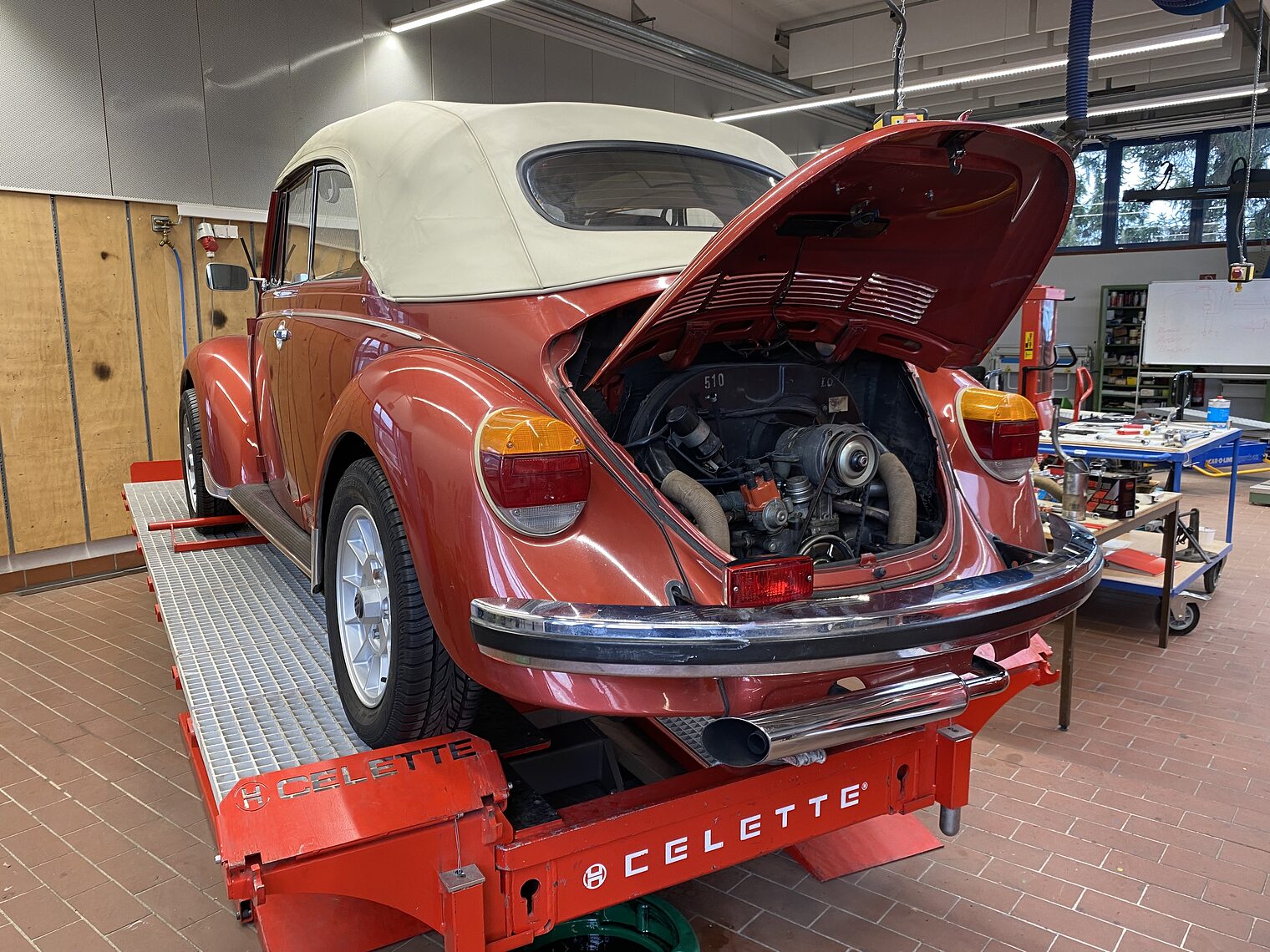 VW Käfer Ein roter VW Käfer mit offenem Motorraum steht in einer Werkstatt auf einer Hebebühne.
