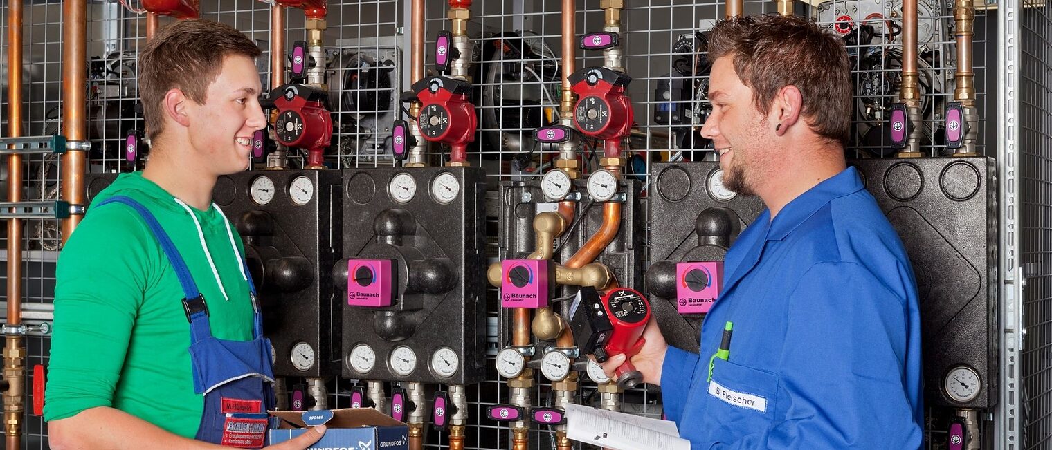 Zwei Männer Anlagenmechaniker/-in für Sanitär-, Heizungs- und Klimatechnik unterhalten sich bei der Arbeit