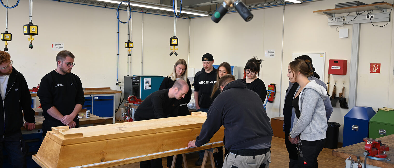 Auszubildende stehen um einen Sarg und messen ihn aus