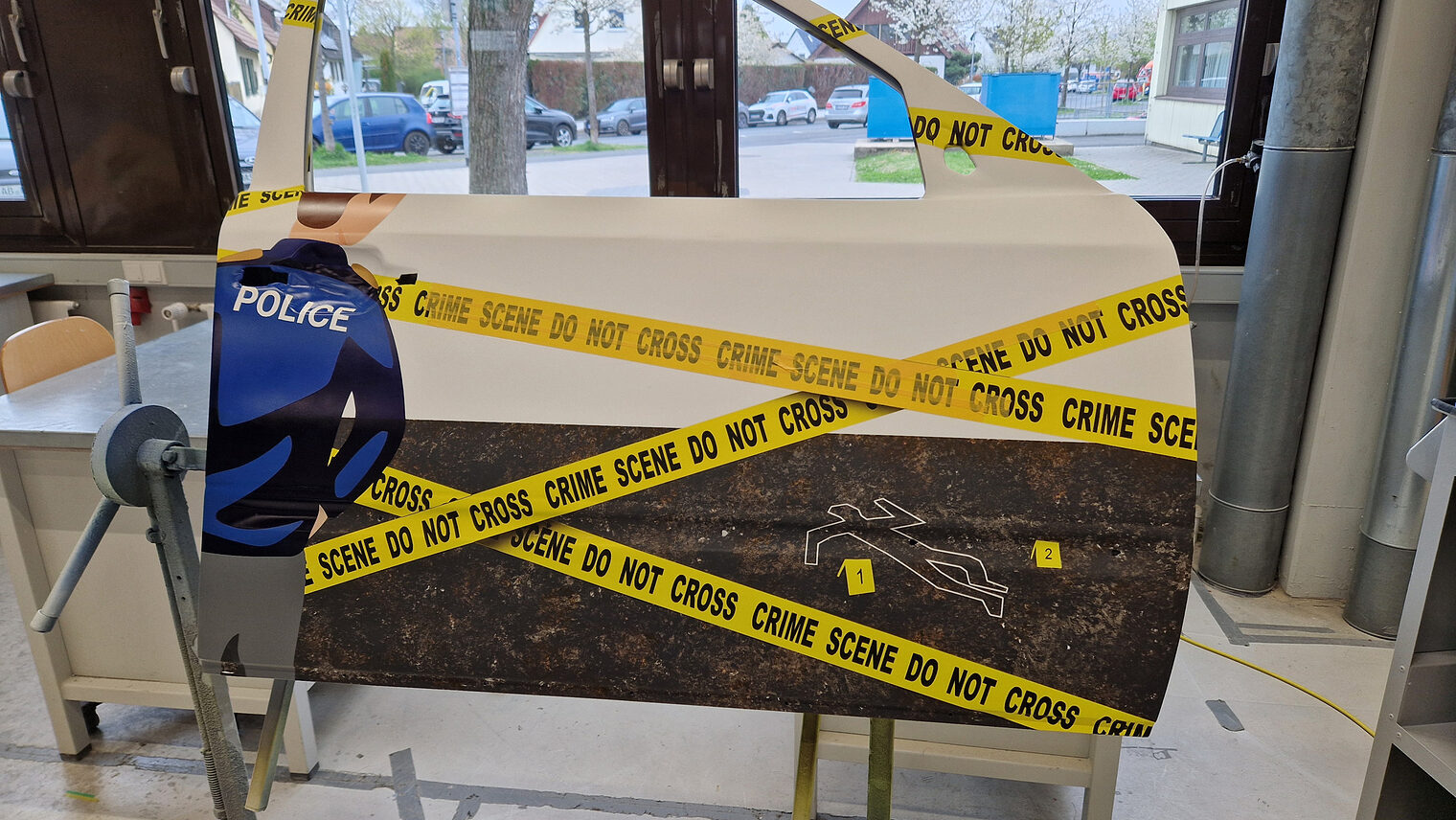 Gesellstück lackierte Autotür, zeigt einen Polizisten und gelbes Absperrband