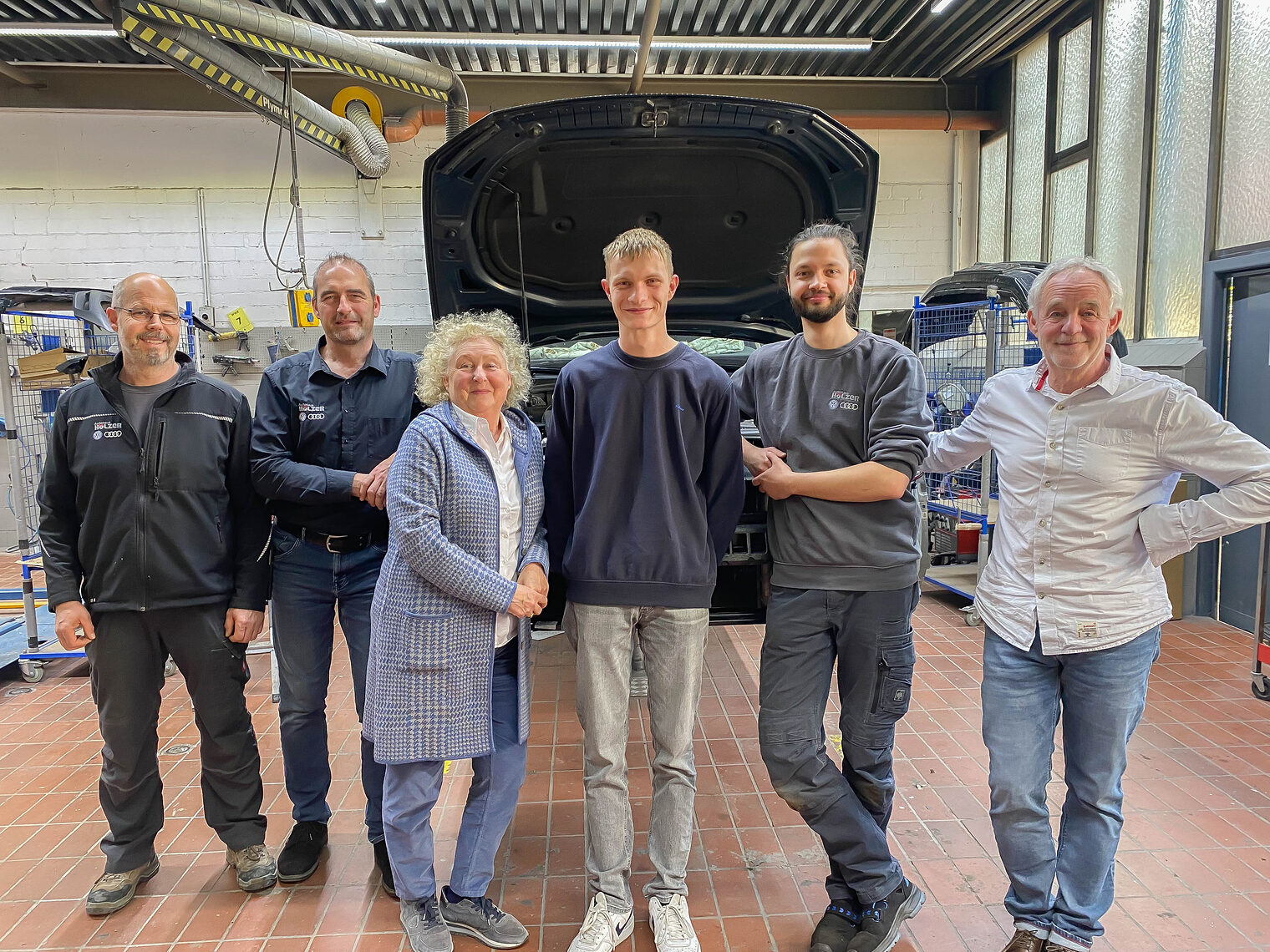 Gruppenbild von 6 Menschen im Stehen in KFZ-Werkstatt, in der Mitte der Kammersieger