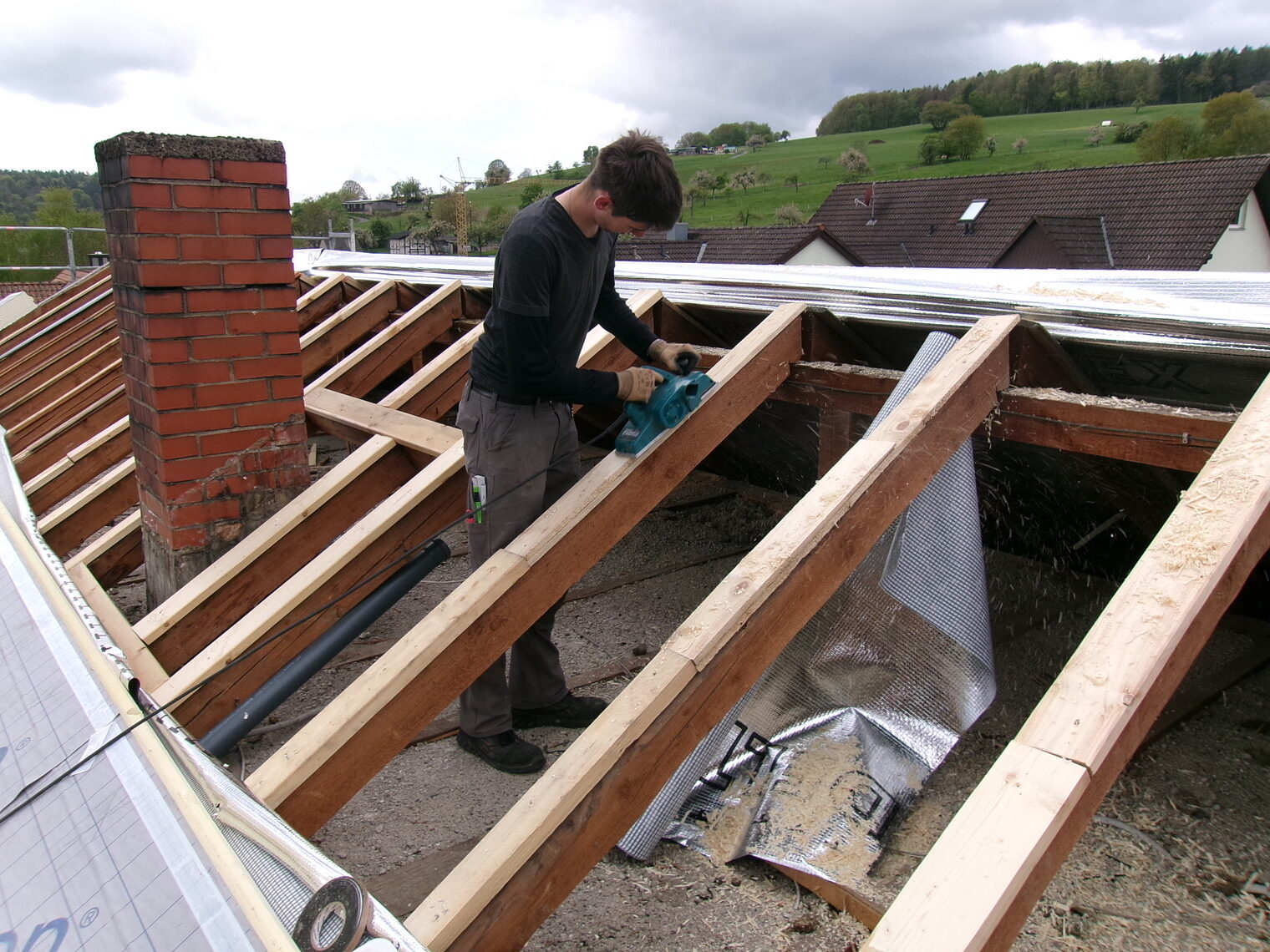 Junger Mann arbeitet im Dachstuhl eines Hauses, Dach ist abgenommen