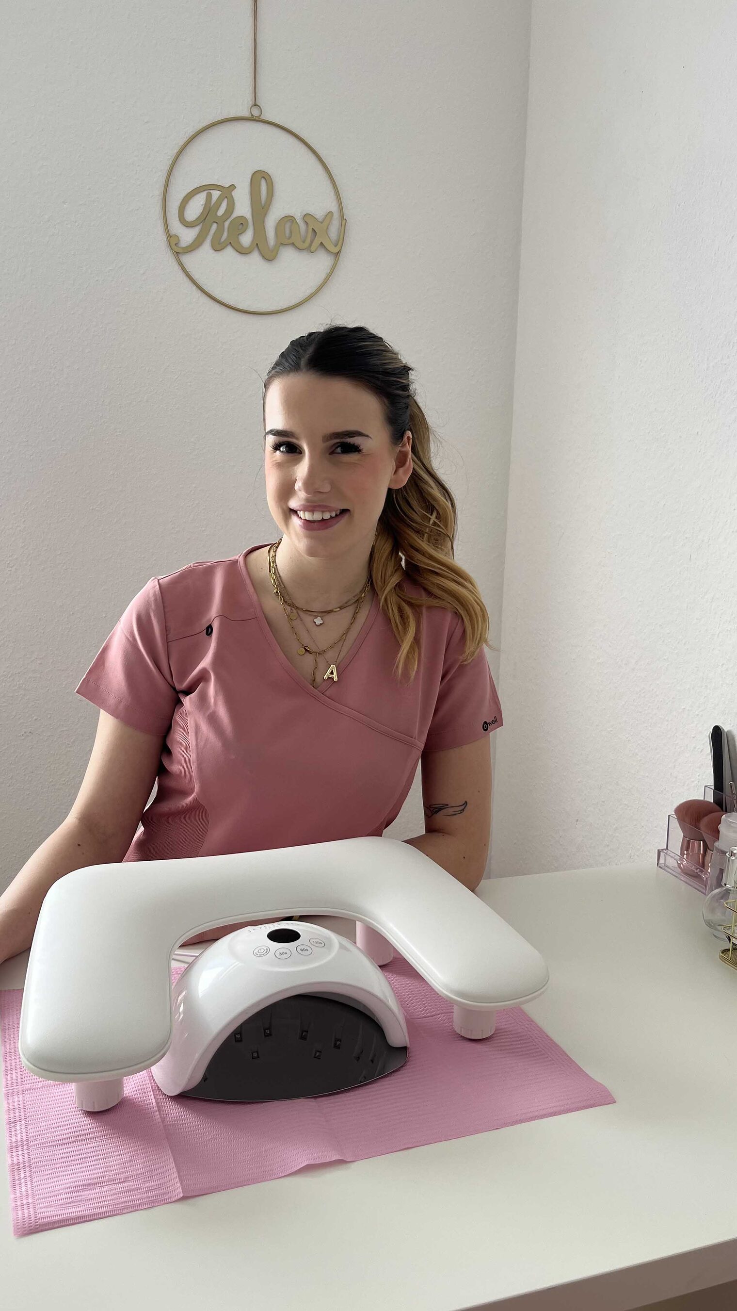 Frau sitz an Tisch mit Nagel-UV-Gerät, lächelt in die Kamera