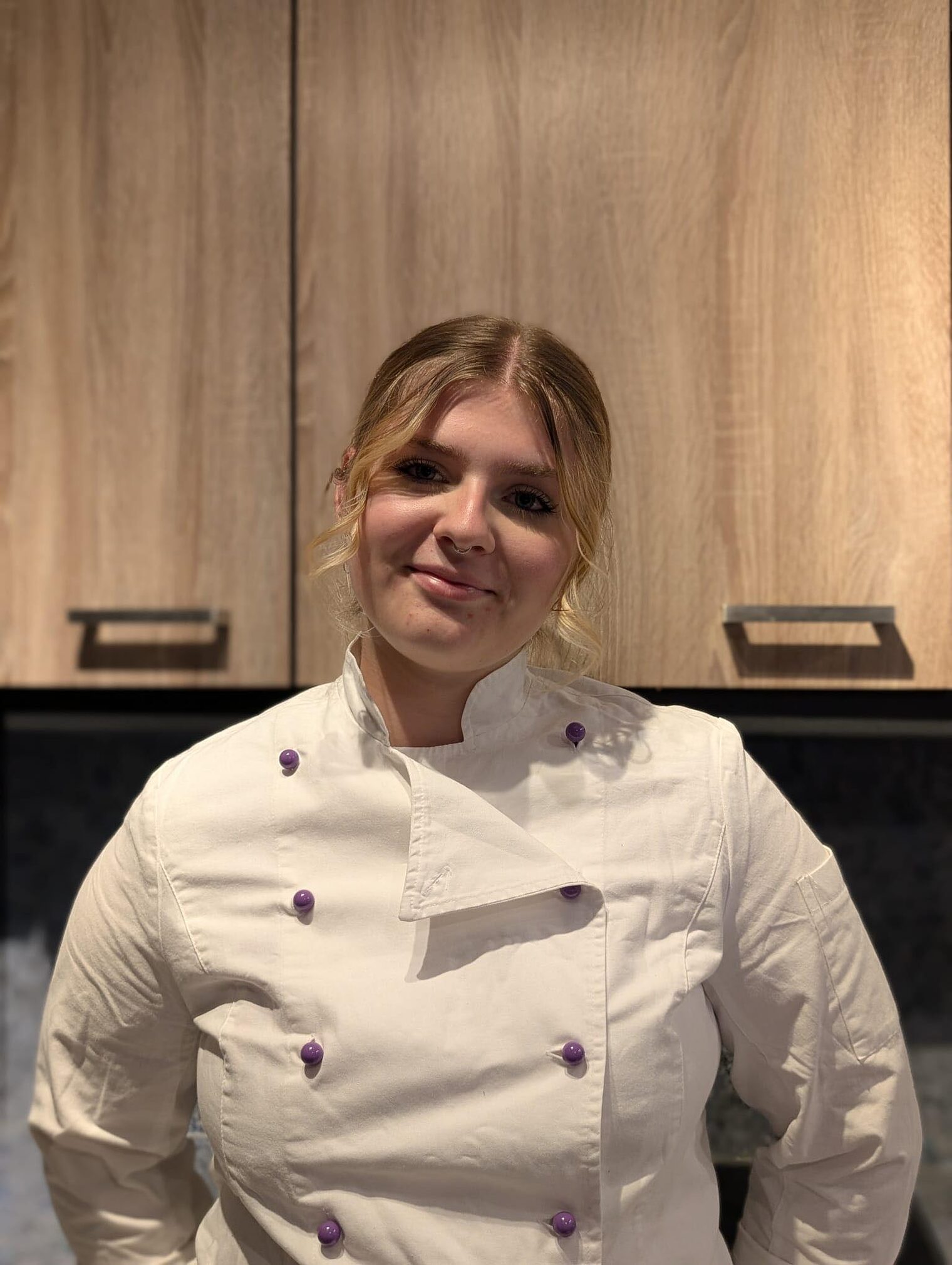 Blonde Frau lächelt in die Kamera, trägt weißes Konditoren-Oberteil