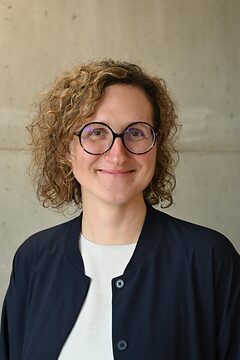 Portrait: Frau mit Locken und runder Brille lächelt in die Kamera