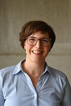 Frau in hellblauer Bluse mit kurzen braunen Haaren lächelt Frau in hellblauer Bluse mit kurzen braunen Haaren lächelt in die Kamera