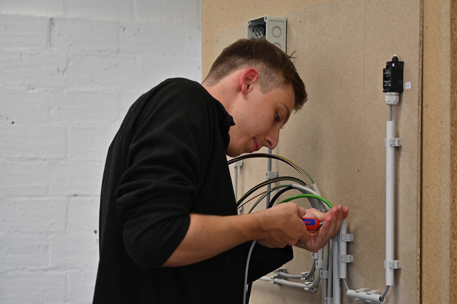 Junger Mann von der Seite, Schraubenzieher in der Hand arbeitet an Verkabelung