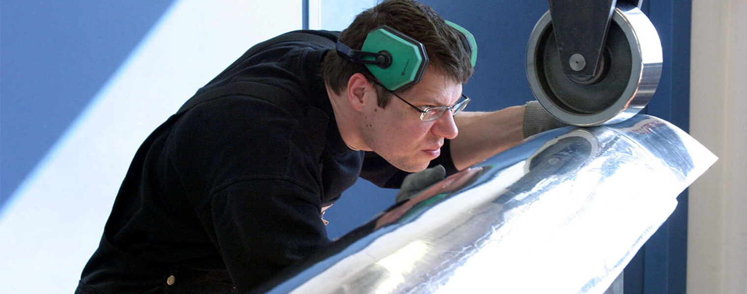 Mann mit grünem Gehörschutz arbeitet an ein einer Rollenstreckmaschine